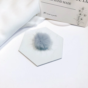 Detailed view of a soft grey mink fur pompom accessory on a white marble coaster