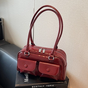 Detail view of a glossy red PU leather handbag with front pockets on a dark sofa