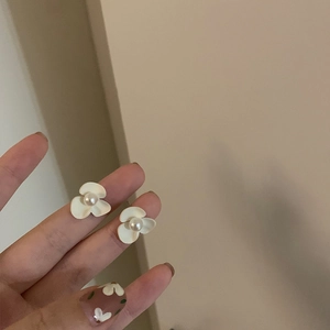 Boucles d'oreilles fleurs blanches avec perle centrale présentées en gros plan à la main