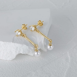 Macro detail of gold S925 silver earring with clear zircon and white dangling pearl