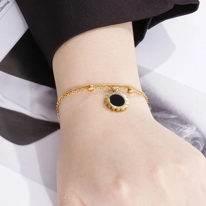 Detail view of double-layer gold snake chain bracelet with black circular pendant