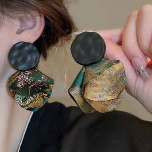 Macro detail of pleated brocade fabric petals and hammered alloy finish earrings