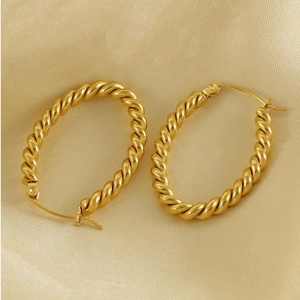 Macro shot of gold oval twist hoop earrings with vintage texture on champagne silk fabric