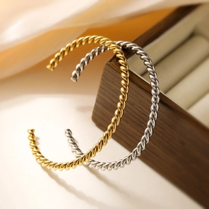 Minimalist 18K gold and silver twisted stainless steel cuff bracelets on wooden jewelry box