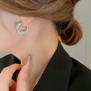 Detail of silver C-shaped earring with woven texture on model in black blazer