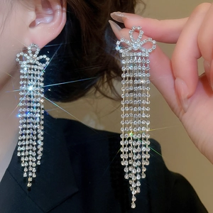 Close-up of sparkling silver tassel earrings with bow design worn on ear with dark background