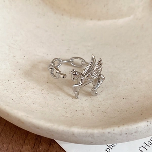 Macro detail of silver Pegasus ring featuring a Cuban link band on a ceramic dish