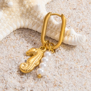 Detail of gold U-shaped earring with seahorse charm and white pearls on white sand