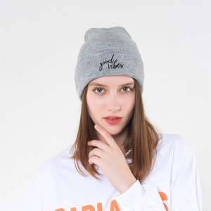 Detail of grey knitted beanie featuring black good vibes embroidery and soft texture