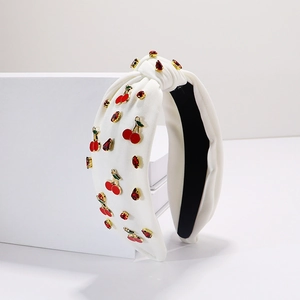 Détail d'un bandeau en tissu blanc avec cerises 3D et ornements en cristal rouge