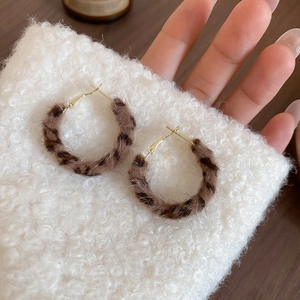 Detail of leopard print faux fur hoop earrings with golden metal studs in hand