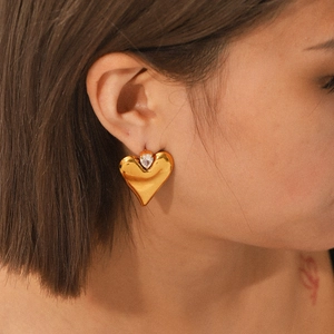Golden heart-shaped stud earrings with sparkling crystals worn on ear for women