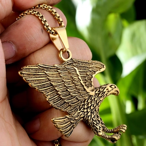 Hand holding a golden eagle pendant necklace in stainless steel with sharp metal details