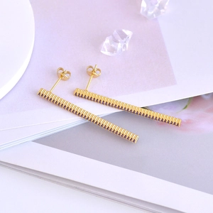 Macro detail of gold bar stud earrings featuring a row of vibrant purple cubic zirconia