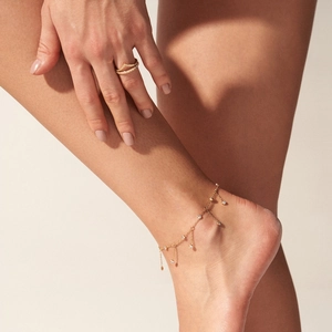 Detailed shot of a gold tassel anklet with zircon pendants worn on a woman's ankle