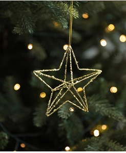 Detail of a sparkling gold star ornament hanging on a Christmas tree with bokeh lights