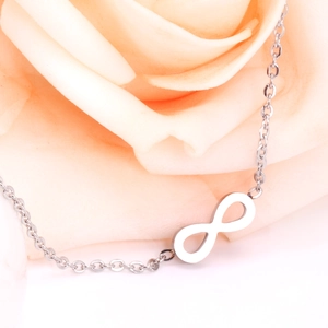 Close-up of infinity symbol pendant on a delicate silver chain with rose petals
