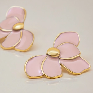 Close-up of pink flower earrings with gold metal edges on a reflective surface