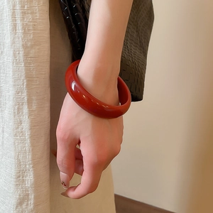 Close-up of a glossy dark red resin bangle worn with a minimalist textured cream outfit