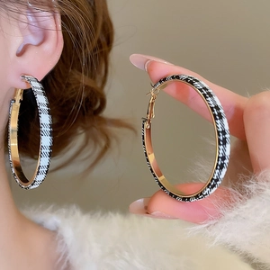 Détail de créoles dorées avec un motif en tissu pied-de-poule noir et blanc chic