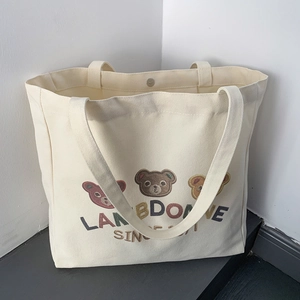 Detail of off-white canvas tote bag featuring embroidered bears and colorful letters