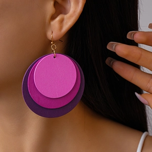 Close-up of geometric layered round wood earrings in gradient purple and pink on a model