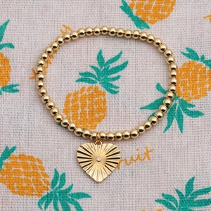 Close-up of gold-plated beaded bracelet with a textured heart charm and white zircon