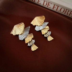 Detail of layered gold and silver fan-shaped earrings with textured radial engravings