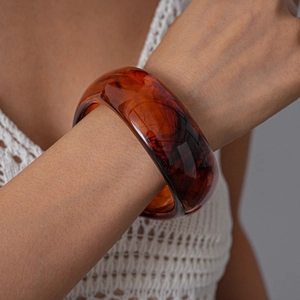 Close-up of wide acrylic bangle with amber tortoiseshell pattern on a model's wrist