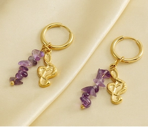 Macro shot of gold music note earrings with purple natural stones on champagne silk fabric