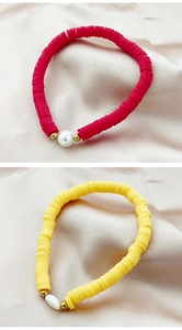 Detail of red and yellow clay bead bracelets with baroque pearls on satin background