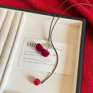 Close-up of velvet cherry pendant with silver leaves on a black cord necklace