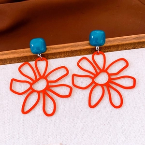 Dettaglio di orecchini vintage con perni blu e ciondoli a fiore arancioni su legno