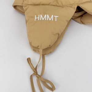 Macro detail of HMMT embroidery on khaki quilted earflaps of a winter aviator hat