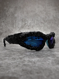 Detailed close-up of avant-garde sunglasses with black textured frame and blue-purple lenses