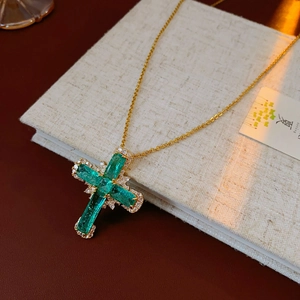 Macro detail of cross pendant with green emerald-cut stones and crystal pavé on gold chain