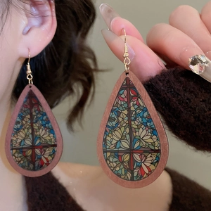 Macro detail of wood teardrop earrings featuring colorful vintage floral stained glass patterns