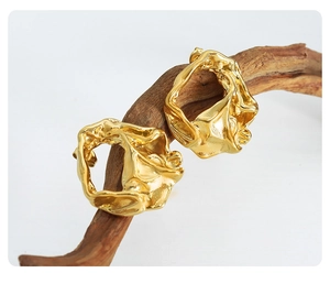 Macro detail of gold-tone earrings with irregular lava texture on wood branch