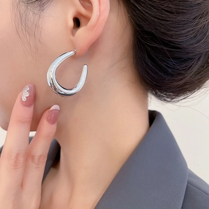 Close-up of polished silver C-shaped hoop earring on model with minimalist modern design