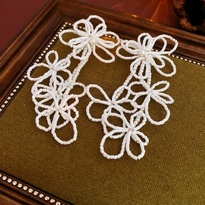 Detail of white beaded flower earrings resting on a vintage green velvet jewelry tray