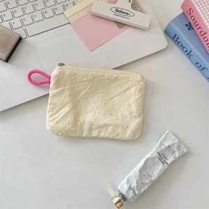 Detailed flat lay of a beige polka dot cosmetic pouch with pink ribbon handle on desk