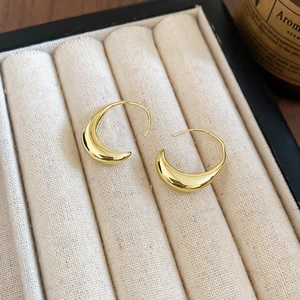 Macro shot of polished 14k gold plated geometric oval crescent hoop earrings on beige display