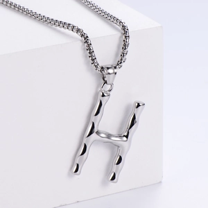 Vue macro du pendentif lettre H argenté avec texture bambou et chaîne à maillons