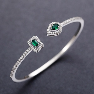 Detailed close-up of silver open bangle with pear and emerald cut green stones