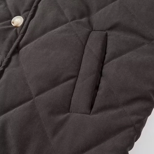 Macro view of black diamond-quilted jacket featuring beige button and vertical pocket detail