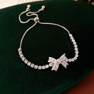 Detail of silver bow bracelet with zircons and adjustable mesh chain on green velvet