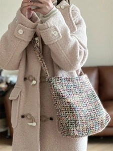 Colorful woven crossbody bag paired with a light pink wool coat featuring toggle buttons
