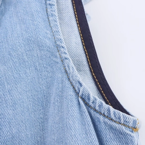 Gedetailleerde close-up van lichtblauwe denimstof met gele contraststiksels en textuur