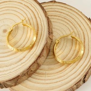 Gold stainless steel hoop earrings with Greek key pattern on natural wooden slices