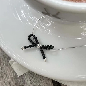 Minimalist 925 sterling silver necklace with black beaded bow pendant on a white porcelain cup